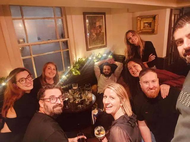 A group selfie around a pub table at Christmas, fairy lights in the window.