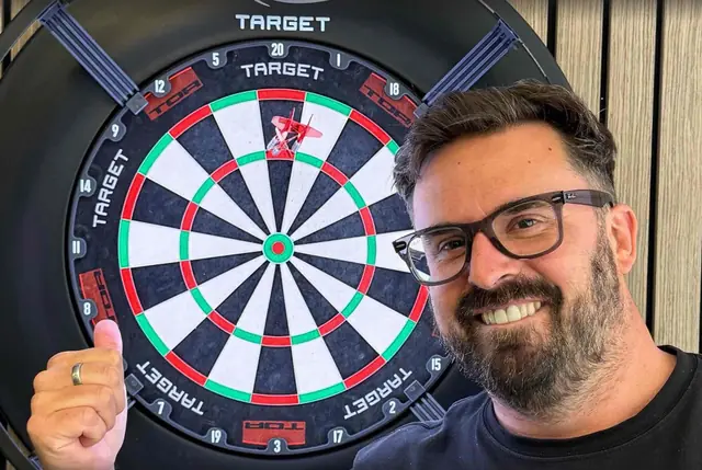 A smiling team member giving a thumbs up beside a dartboard, dart in the 20.