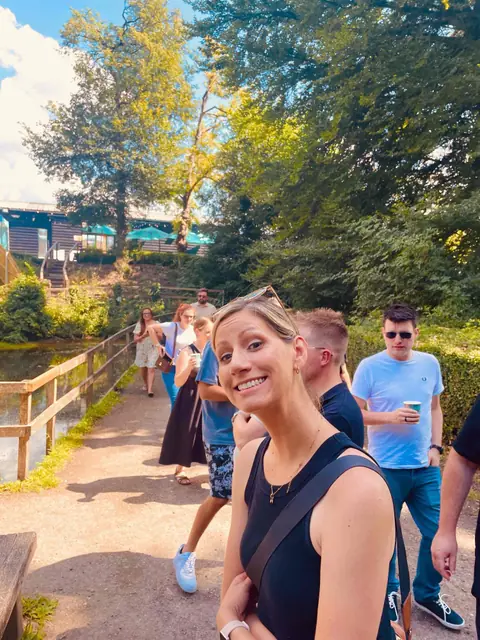 A colleague grinning at the camera on a lakeside path, the team walking behind her.