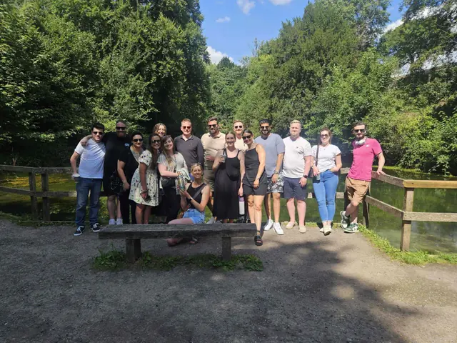 The whole team posing by a fence beside a lake, surrounded by trees.