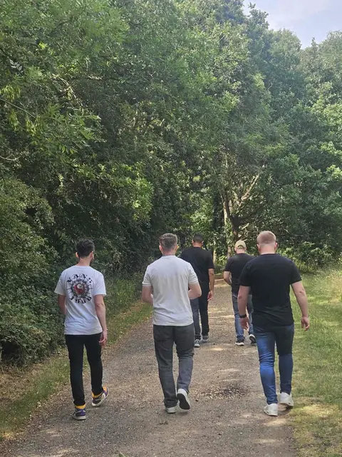 Five colleagues walking away down a woodland path.